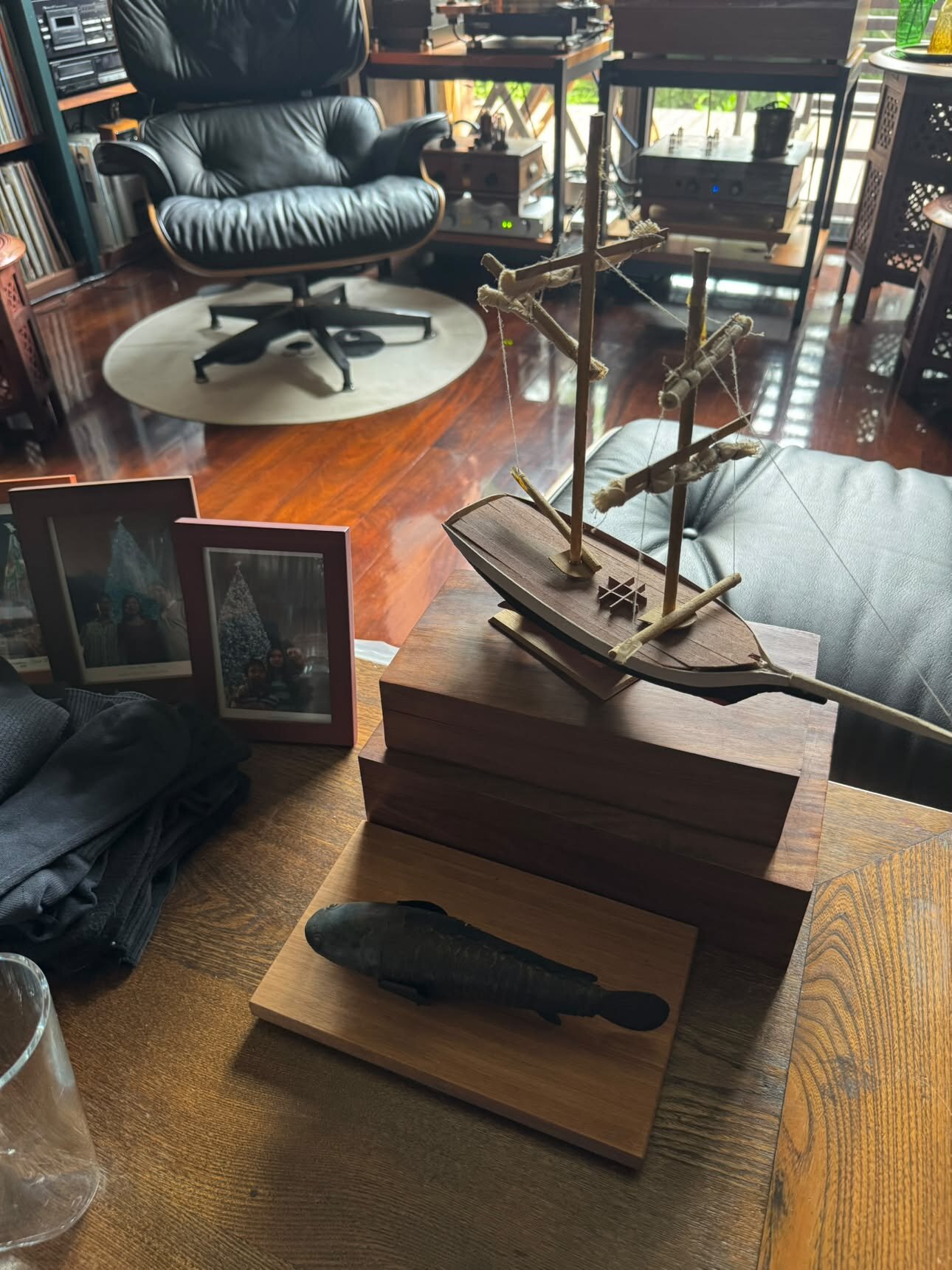 Petit bateau en bois de balsa posé sur des boîtes en bois, fauteuil Eames en arrière-plan, cadres photo de famille