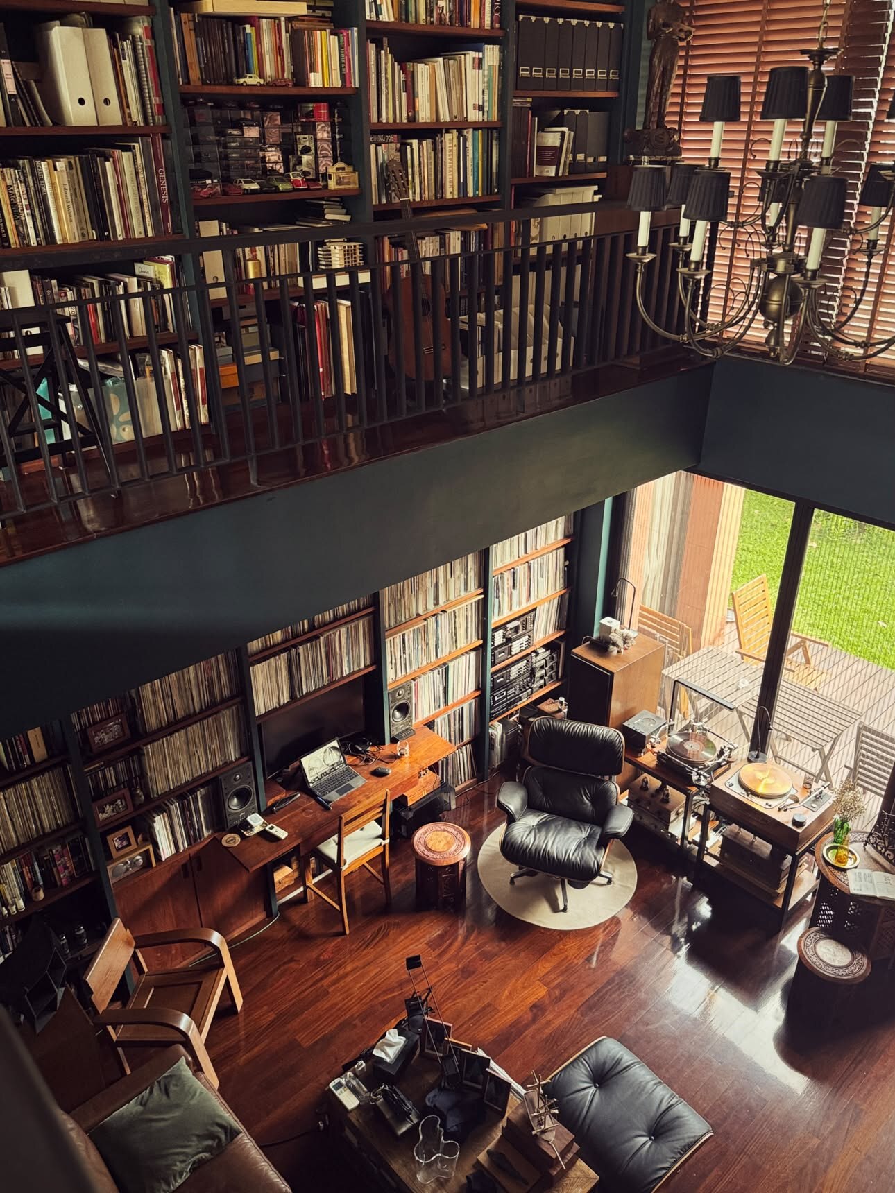 Vue depuis la mezzanine des livres, murs de disques et cassettes sur deux étages, baie vitrée sur le jardin en contrebas
