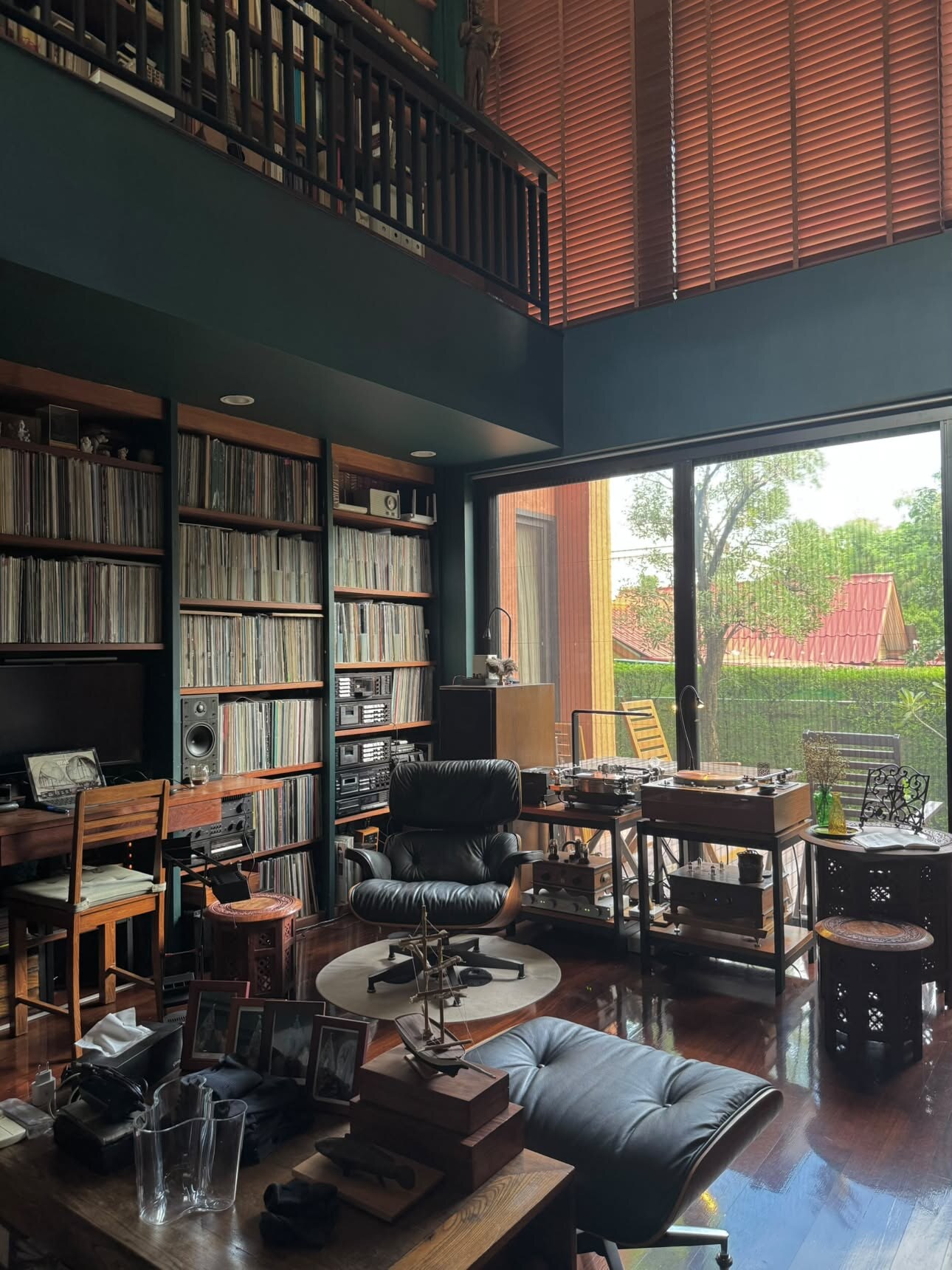 Vue générale de la pièce depuis un angle haut, mezzanine de livres, murs de disques sur deux étages, baie vitrée sur le jardin