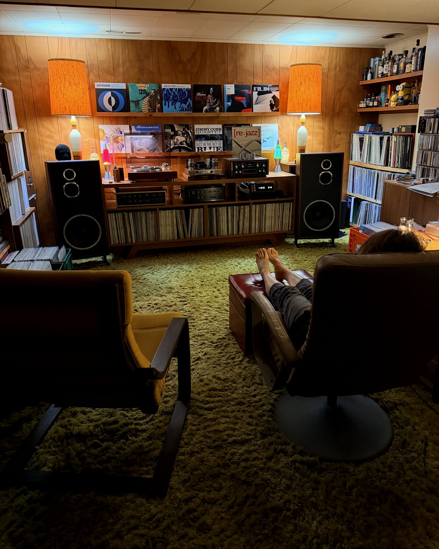 Pieds nus posés sur un pouf en cuir, vue depuis les deux fauteuils face au meuble hi-fi, tapis shag vert