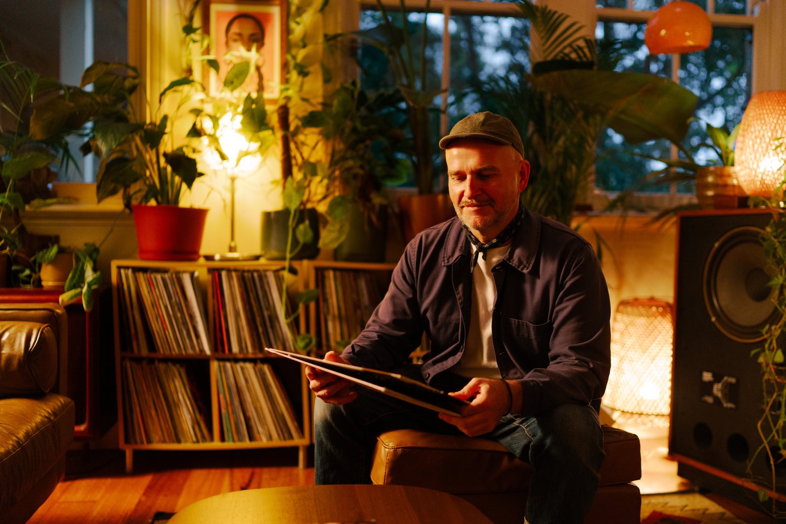 Eddie assis sur le pouf, un disque entre les mains, bibliothèque de vinyles et plantes en fond