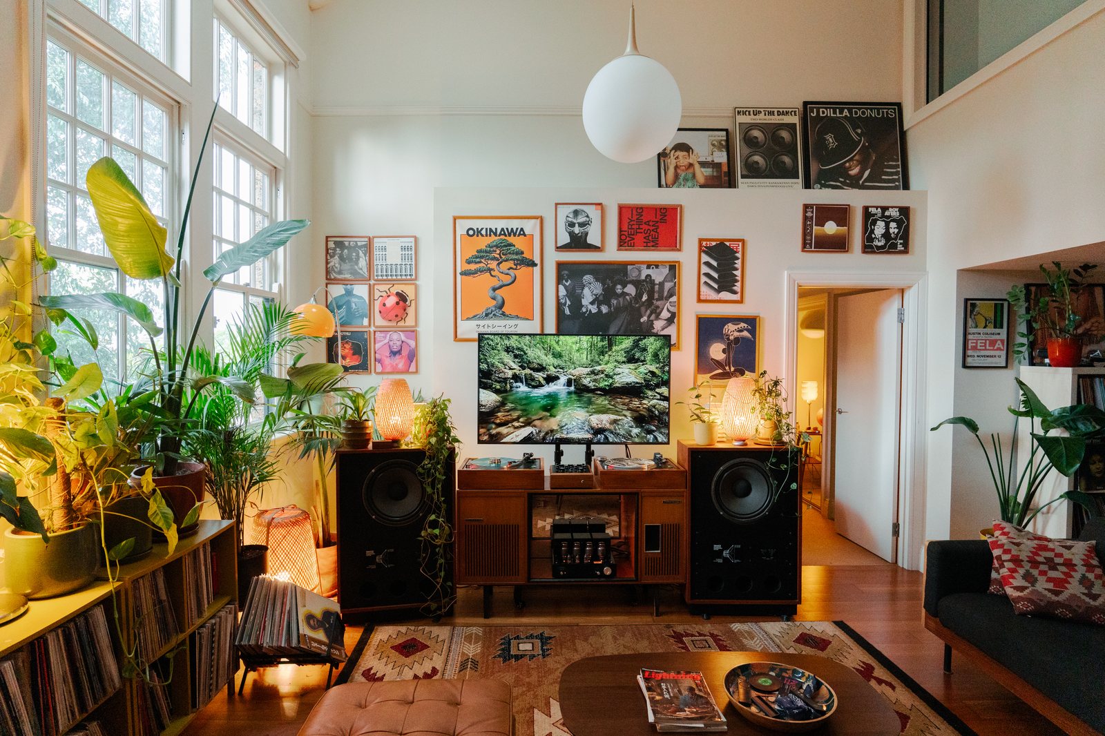 Vue large du salon depuis le canapé en cuir, mur de pochettes encadrées, plantes